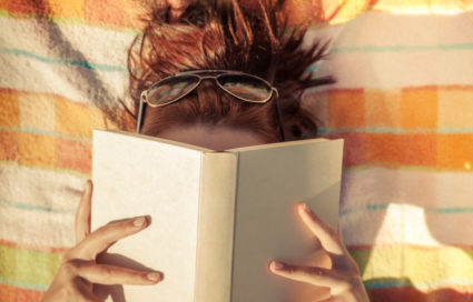 Woman reading book on beach blanket