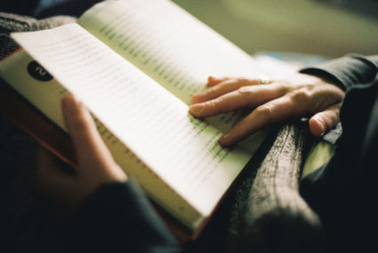 close-up of a woman reading a book, with soft indoor light hitting her hands holding the open book.