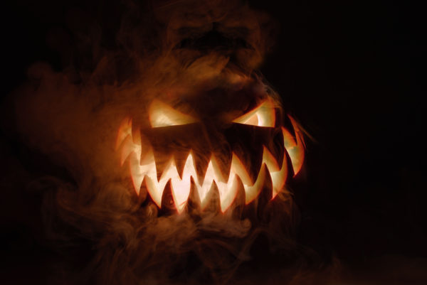 Fuming bright Jack-o'-lantern pumpkin on dark solid background. Glowing eyes and a terrible grin. Halloween minimal concep...