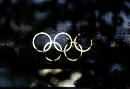 The giant Olympic rings are seen through a tree in the dusk in Tokyo