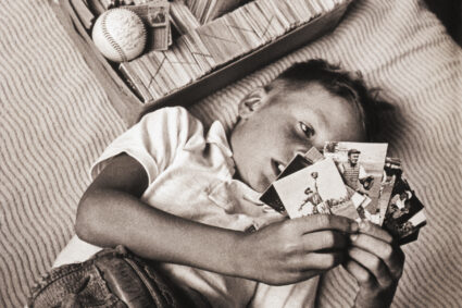 Boy Lying on Bed Studying Baseball Cards